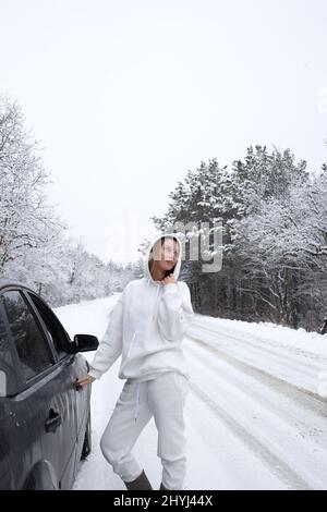 la giovane donna apre la porta dell'auto sullo sfondo di un paesaggio innevato Foto Stock