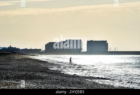 Brighton UK 7th Marzo 2022 - un nuotatore di prima mattina si dirige verso il mare sulla spiaggia di Brighton in una bella giornata di sole con le previsioni del tempo caldo per spargersi in tutta la Gran Bretagna nei prossimi giorni : Credit Simon Dack / Alamy Live News Foto Stock