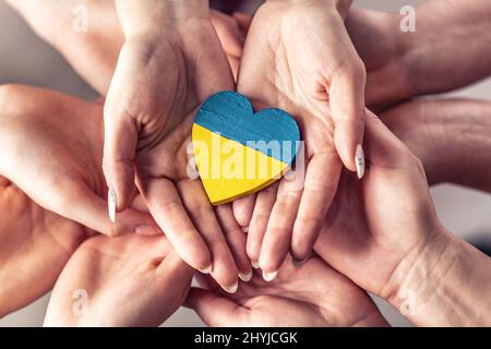 Ci troviamo con il simbolo dell'Ucraina, poiché numerose mani si tengono in unità con un cuore di legno dipinto in colori della bandiera Ucraina sulla parte superiore. Foto Stock