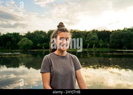 Portait di donna sorridente con prechi nel parco, sfondo lago. Foto Stock