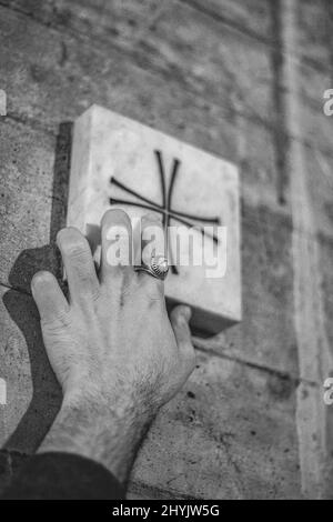 Primo piano verticale in scala di grigi della mano dell'uomo che tocca la croce. Foto Stock