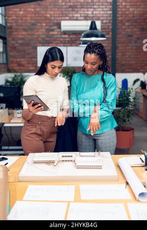 Giovani architetti multirazziali che puntano sul modello di costruzione mentre discutono sul tablet digitale Foto Stock