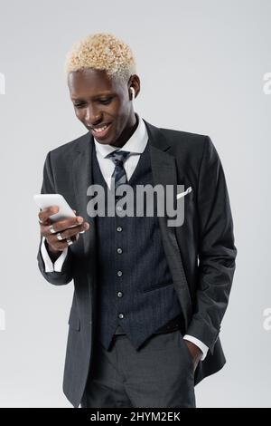 felice uomo afroamericano in auricolari wireless utilizzando smartphone isolato su grigio Foto Stock