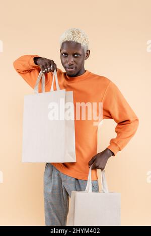 giovane uomo afroamericano in felpa arancione con borse per lo shopping isolate sul beige Foto Stock