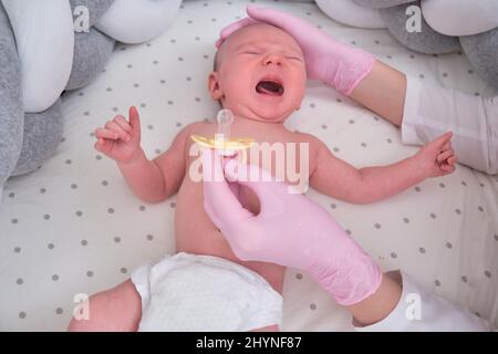 Il medico dona un succhietto a un neonato. L'infermiera in uniforme lenisce un bambino piangendo Foto Stock