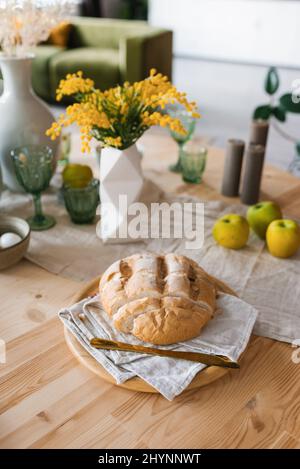 Una pagnotta di pane fresco sul tavolo della colazione, fiori mimosa in vaso Foto Stock