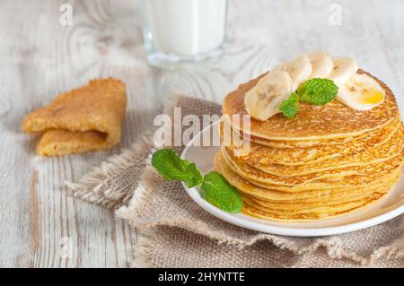 Pancake serviti con latte, guarniti con foglie di menta e fette di banana. Versare con miele o sciroppo d'acero. Foto Stock