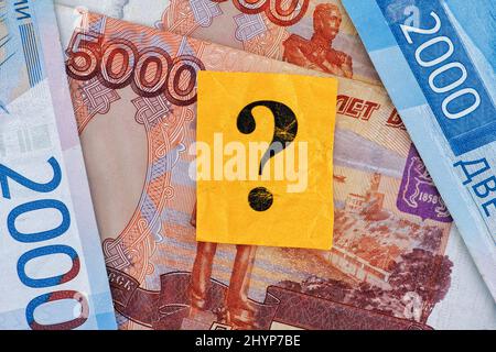Un pezzo di carta giallo con un punto interrogativo su di esso e qualche ruble banconote sotto di esso. Primo piano. Foto Stock