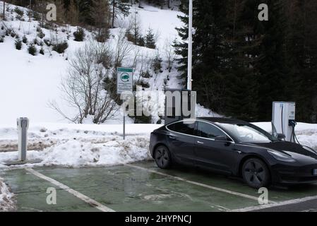 Brennero, Italia - 18 febbraio 2022: Uno scatto statico di una carica awd a lungo raggio a doppio motore Tesla modello 3 a nero solido alla carica rapida CC in una nuvola Foto Stock