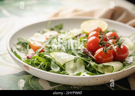 Insalata verde di primavera con rucola, cetrioli e pomodori su sfondo piastrellato. Piatto vegano vegetale sano. Foto Stock
