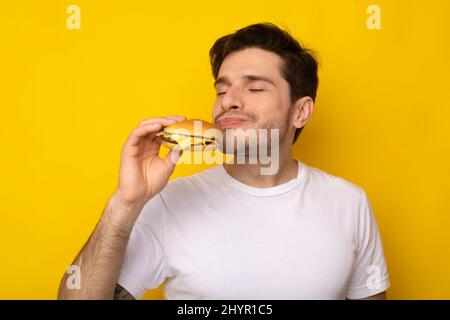 Primo piano del Guy eccitato che mangia il Burger gustoso allo Studio Foto Stock