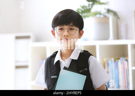 Laurea, ingresso e nuovo semestre Un ragazzo carino e intelligente che porta uno zaino e sorridente va a scuola con un libro. Foto Stock