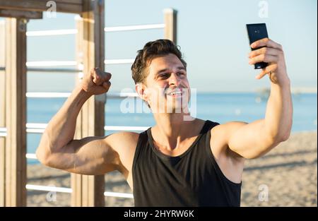 Uomo allegro mostrando bicipiti prendendo selfie Foto Stock