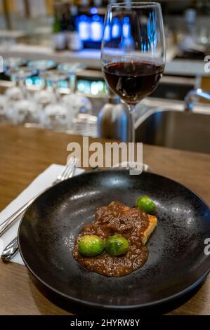 Piatti spagnoli, tortilla di patate con salsa di carne e germogli di bruxelles serviti con un bicchiere di vino rosso tempranillo spagnolo secco da vicino Foto Stock