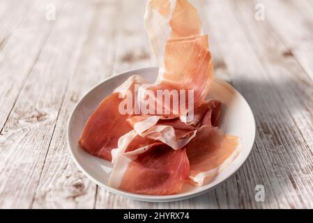 Prosciutto di Parma a fette in piatto bianco su tavola di legno, vista dall'alto Foto Stock