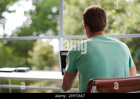 Navigare sul Web con una vista. Scatto retroguarato di un giovane uomo con un computer portatile a casa. Foto Stock