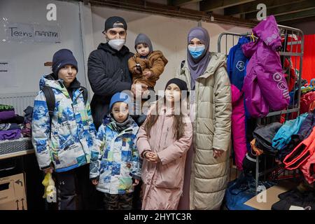 15 marzo 2022, Amburgo: La famiglia di rifugiati ucraini di Mohamed Jazara e Ludmilla Stupka con i loro figli Adam (l-r), Amin (5), Abdulla (1) e Jasmina (8) si trova nel negozio di abbigliamento di Rissen. Mohamed Jazara era già fuggito dalla Siria, poi dalla Crimea e, più recentemente, da Odessa. Ludmilla Stupka proviene da Donetsk. L'Arbeiter-Samariter-Bund (ASB) organizza il più grande negozio di abbigliamento di Amburgo attraverso il suo capitolo Amburgo-Mitte. La cosa speciale di questo progetto è che gli sfollati ucraini di guerra e i volontari di Amburgo riempiono e organizzano il negozio di abbigliamento insieme e cercano il suitabl Foto Stock