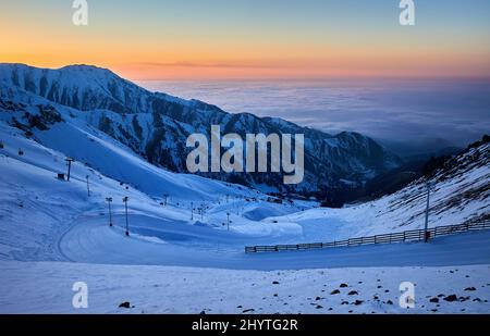 Bellissimo paesaggio Shymbulak montagna resort nevoso neve vuoto pista da sci e funivia ascensore al tramonto cielo arancione in Almaty, Kazakhstan. Foto Stock