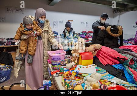 15 marzo 2022, Amburgo: La famiglia di rifugiati ucraini di Mohamed Jazara (r) e Ludmilla Stupka con i loro figli Abdulla (l) e Adam si trovano nel negozio di abbigliamento di Rissen in cerca di vestiti. Mohamed Jazara era già fuggito dalla Siria, poi Crimea e, più recentemente, Odessa. Sua moglie viene da Donetsk. L'Arbeiter-Samariter-Bund (ASB) organizza il più grande negozio di abbigliamento di Amburgo attraverso il suo capitolo Amburgo-Mitte. La cosa speciale di questo progetto è che gli sfollati ucraini di guerra e i volontari di Amburgo riempiono e organizzano il negozio di abbigliamento insieme e cercano gli articoli adatti di cl Foto Stock