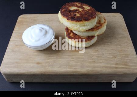 colazione casolare formaggio frittelle cheesecake su un vassoio di legno con salsa bianca panna acida. Russo sano piatto da colazione cottage formaggio cibo sano Foto Stock