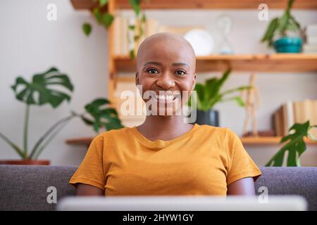 Una giovane donna si siede sul divano con il suo laptop e sorride Foto Stock