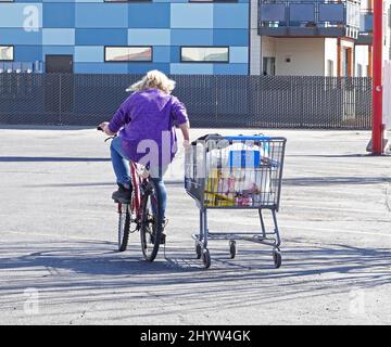 Una persona senza tetto su una bicicletta che tira un carrello di shopping del negozio di alimentari riempito di generi alimentari gratuiti. Oregon Foto Stock