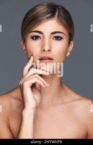 Pelle incredibilmente morbida. Un ritratto corto di una bella giovane donna che toching il suo volto isolato su grigio. Foto Stock