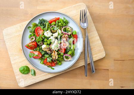 Pasto vegetale a base di fagioli verdi, piselli e spinaci con cipolle brasate, formaggio feta e pomodori per una dieta vegetariana a basso contenuto di carb su un tavolo di legno, poliziotto Foto Stock