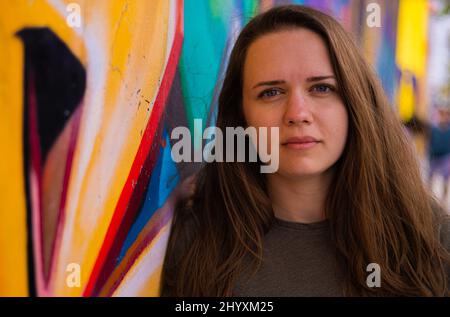 Giovane e bella donna si appoggia contro un muro colorato e si pone per la macchina fotografica - stile di strada tipico Foto Stock