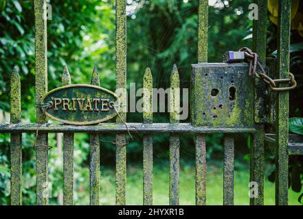 Una porta in ferro arrugginita con la parola privata su una targa, chiusa e fissata con un lucchetto e una catena. Foto Stock