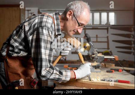 Carpentiere esperto che intagliano legno con martello e scalpello. Fotografia di alta qualità Foto Stock