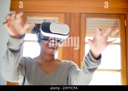 Ritratto di una giovane donna nera attiva che prova un simulatore di realtà virtuale in una stanza a casa. Concetti di tecnologia e stile di vita. Foto Stock