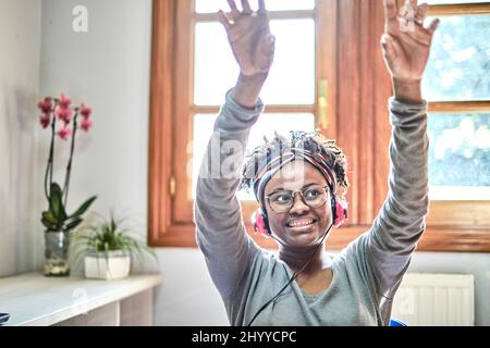 Giovane donna nera con acconciatura afro che ascolta la musica con le cuffie in casa. Concetto di stile di vita. Foto Stock