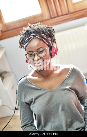 Giovane donna nera con acconciatura afro che ascolta la musica con le cuffie in casa. Concetto di stile di vita. Foto Stock