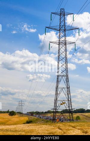 Linee elettriche di alimentazione e auto stradali in fila su un'autostrada o superstrada con le nuvole blu del cielo e il sole Foto Stock