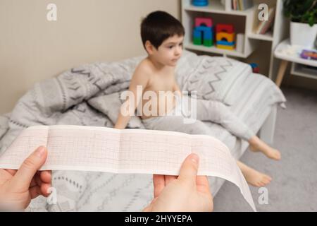 Pellicola ECG nelle mani di un cardiologo pediatra sullo sfondo di un ragazzo di 4 anni. Malattie cardiache nei bambini Foto Stock