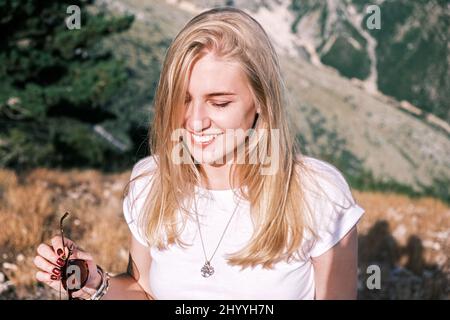 Ritratto fiducioso giovane allegra sorridente donna bionda sullo sfondo delle colline in una giornata di sole. La ragazza felice sorride ampiamente Foto Stock