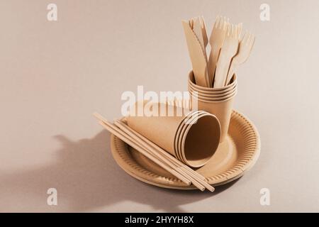 Utensili usa e getta ecocompatibili realizzati in carta artigianale su sfondo beige chiaro. Forche, coltelli, piastre, bicchieri e cannucce Foto Stock