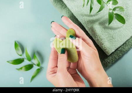 Donna massaggio tenuta mano gua sha raschietto per il viso di pietra di giada verde. Massaggio viso di bellezza, concetto SPA self-care. Foto Stock