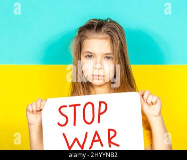 Una ragazza sta piangendo, tenendo in mano un manifesto DI FINE GUERRA contro lo sfondo della bandiera Ucraina. Foto Stock