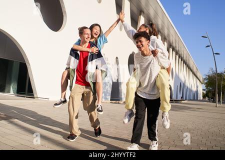 Amici Centennials in vacanza che hanno piggyback e accatastarsi le mani sulla strada della città - gruppo di giovani che godono il tempo insieme ridendo all'aperto. Foto Stock