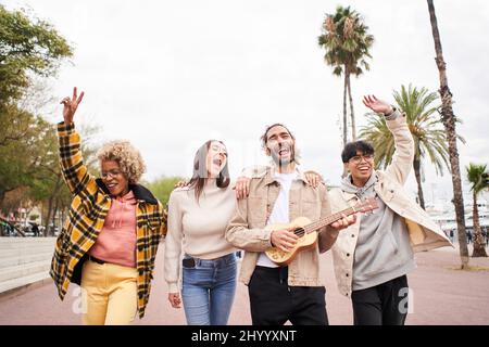 Gente felice che canta e balla all'aperto. Gruppo di amici che si divertono in una festa di giorno che gioca l'ukulele. Foto Stock