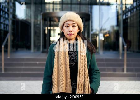 Giovane donna asiatica seria che guarda la macchina fotografica. Signora cinese all'aperto vicino a edifici corporativi in città Foto Stock