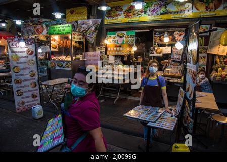 Un venditore attende i clienti di fronte ad un ristorante a Bangkok's Chinatown. Chinatown, conosciuta anche come Yaowarat, è la famosa destinazione per i turisti di notte, con molte bancarelle di cibo di strada e ristoranti cinesi. Foto Stock