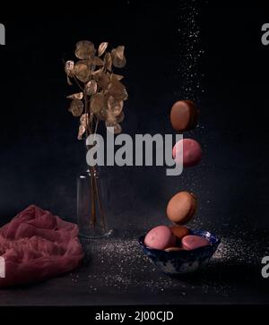 Diverse torte di fusione multicolore cadono in un vaso di paglia con un bouquet di fiori secchi su sfondo nero Foto Stock