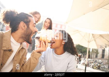 Scena romantica di una coppia che condivide un pasto il loro primo giorno, mentre gli amici guardare sullo sfondo Foto Stock