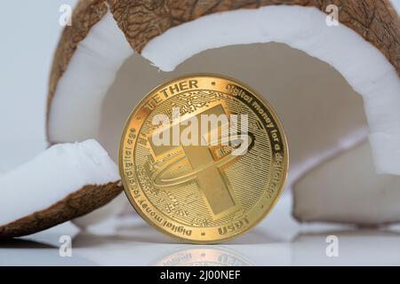 Modulo di raccordo USDT criptovaluta moneta fisica posto accanto a cocco rotto sul tavolo bianco riflettente. Scatto macro. Foto Stock