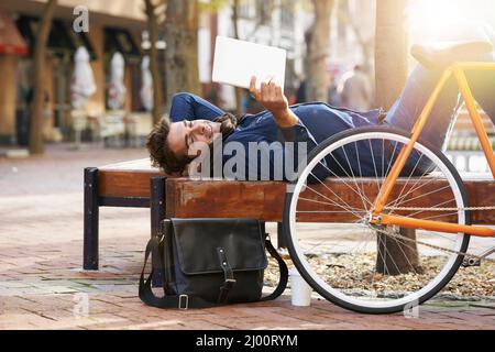 Spensierati in città. Scatto di un uomo usando il tablet mentre fa una pausa in città con la bicicletta accanto a lui. Foto Stock