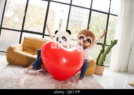 Due donne irriconoscibili con maschera animale orso panda che tiene grande cuore a casa - San Valentino festeggiamenti Foto Stock