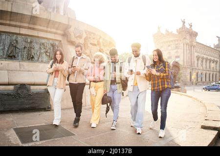 Gruppo di giovani felici che usano i telefoni all'aperto mentre camminano e sorridono. Foto Stock